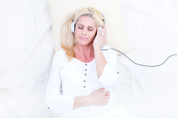 Žena s sluchátka v posteli — Stock fotografie